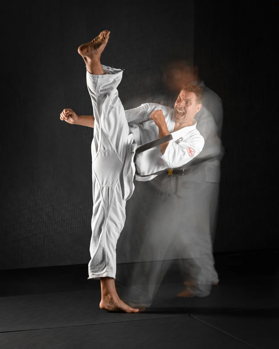Sensei Alexandre Haché : coup de pied haut Sensei Alexandre Haché exécute un coup de pied haut, la jambe à la verticale ; la photo garde la trace du mouvement.