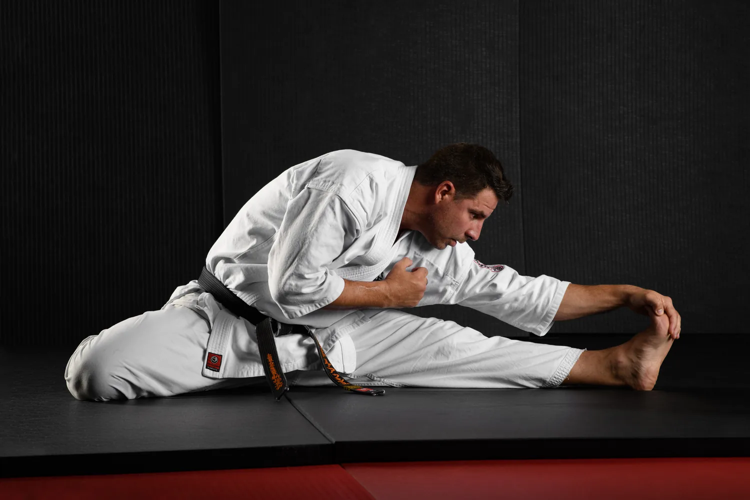 Sensei Alexandre Haché : étirement Sensei Alexandre Haché, assis sur le tatami, étire une jambe tendue et saisit son pied.
